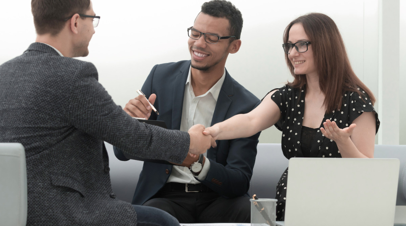 Two men and a women in a business setting, shaking hands.