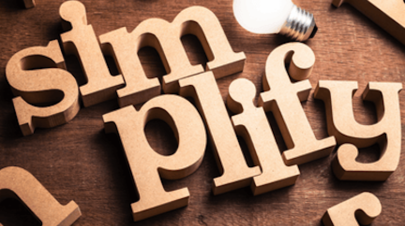 Wooden block letters spelling out the word simplify with an adjacent light bulb