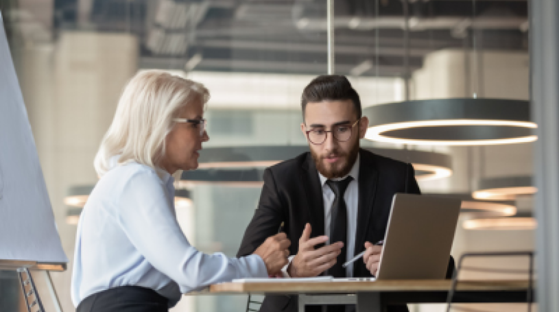 Business man and woman talking at a table in front of a laptop.